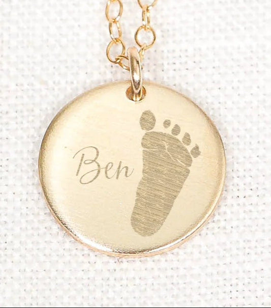 Gold necklace with a round pendant featuring a footprints design and the name.
