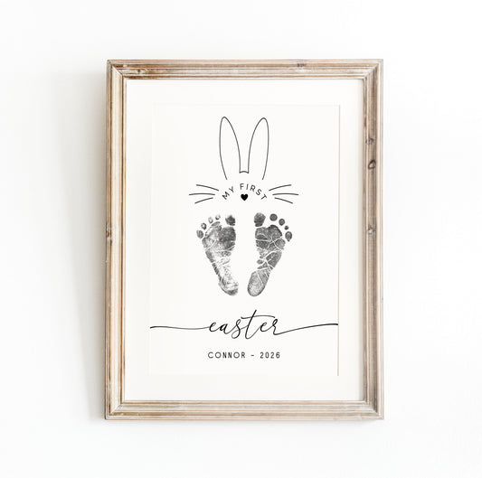 Framed print keepsake with bunny ears, baby footprints, and text on a white background