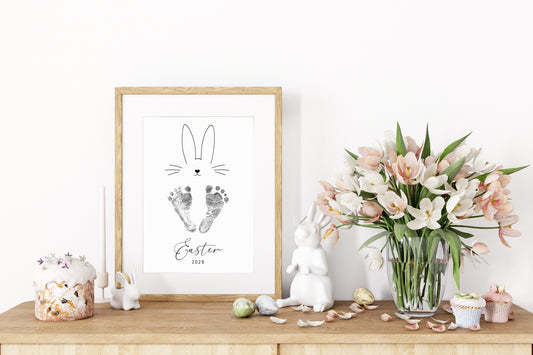 Framed Easter-themed keepsake with baby footprints, bunny, and flowers on a wooden surface.