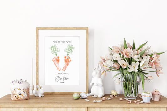 Easter-themed decor with a framed baby footprint keepsake, flowers, and small decorations on a wooden surface.
