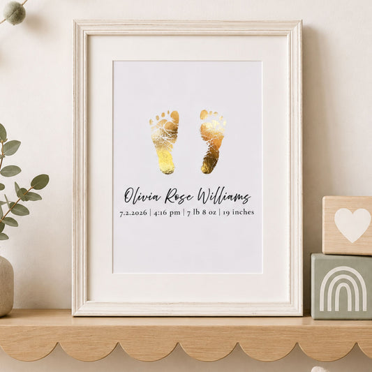 A framed personalized baby footprint print keepsake with gold foil footprints and the name 'Olivia Rose Williams' displayed on a light wood shelf, styled with a plant and wooden blocks.