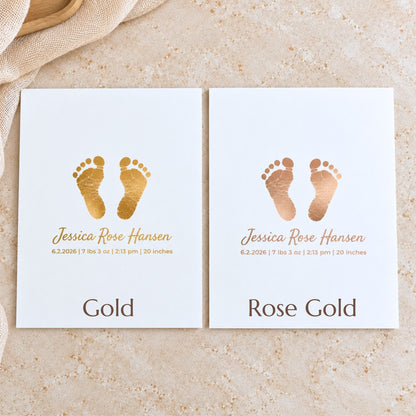 Two white baby keepsake cards with gold foil footprints and personalized names, displayed side by side on a textured beige stone surface with a beige fabric corner.