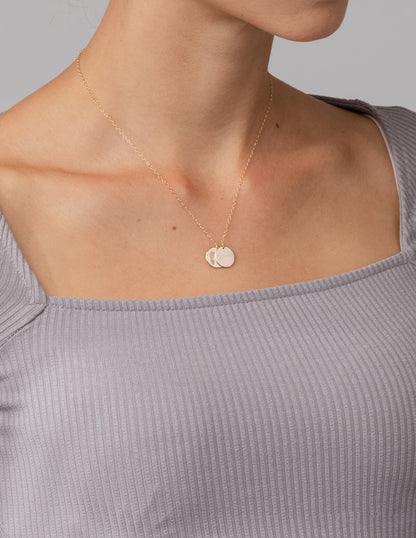 Necklace with round pendants on a person wearing a light gray top against a neutral background