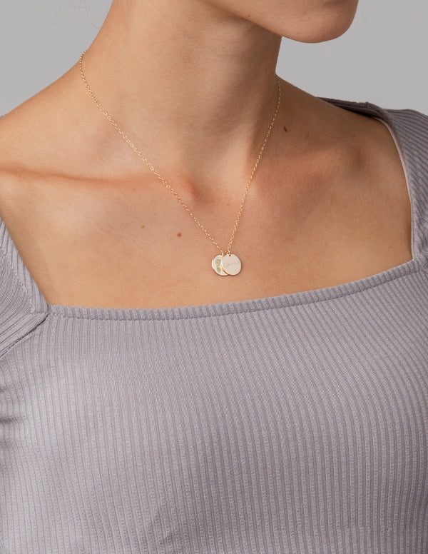 Necklace with round pendants on a person wearing a light gray top against a neutral background
