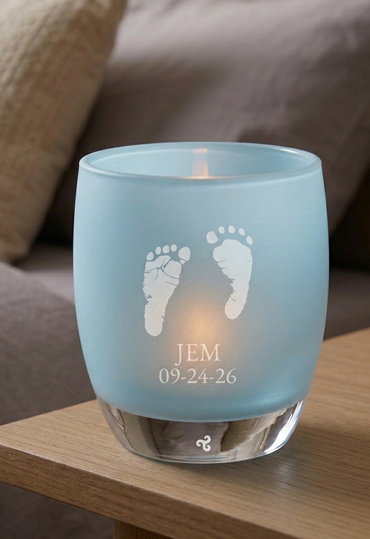 Blue candle holder with engraved baby footprints and name on a wooden table.