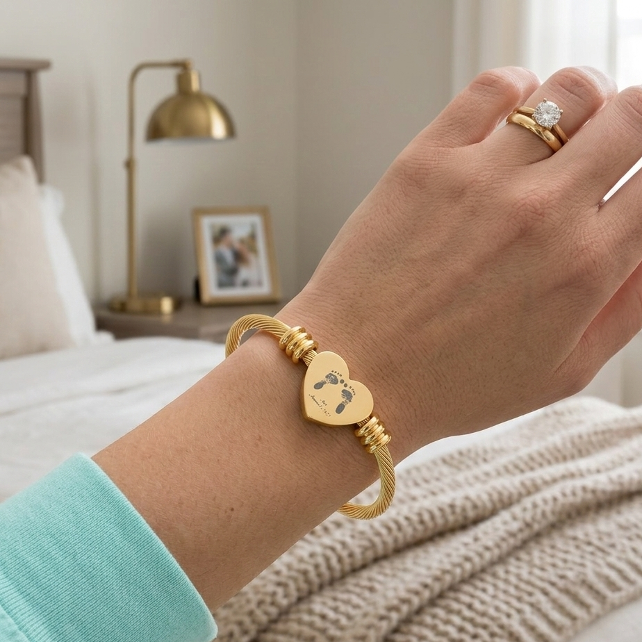 Hand wearing a gold heart-shaped bracelet with a baby footprints on it.