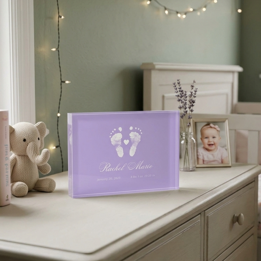 Nursery with a purple keepsake of baby's footprints, teddy bear, and books on a dresser.